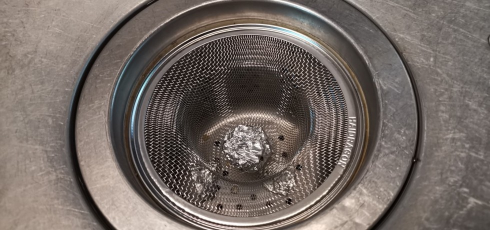 廚房水槽排水濾網上方放一個不鏽鋼濾網，並且在濾網上放上一顆圓形鋁箔球